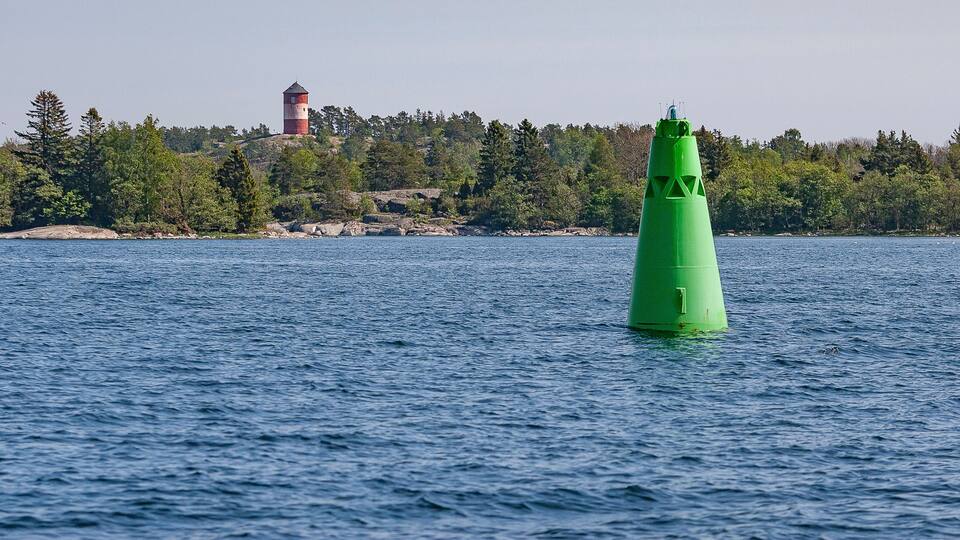 A green buoy in the water with a lighthouse in the background.