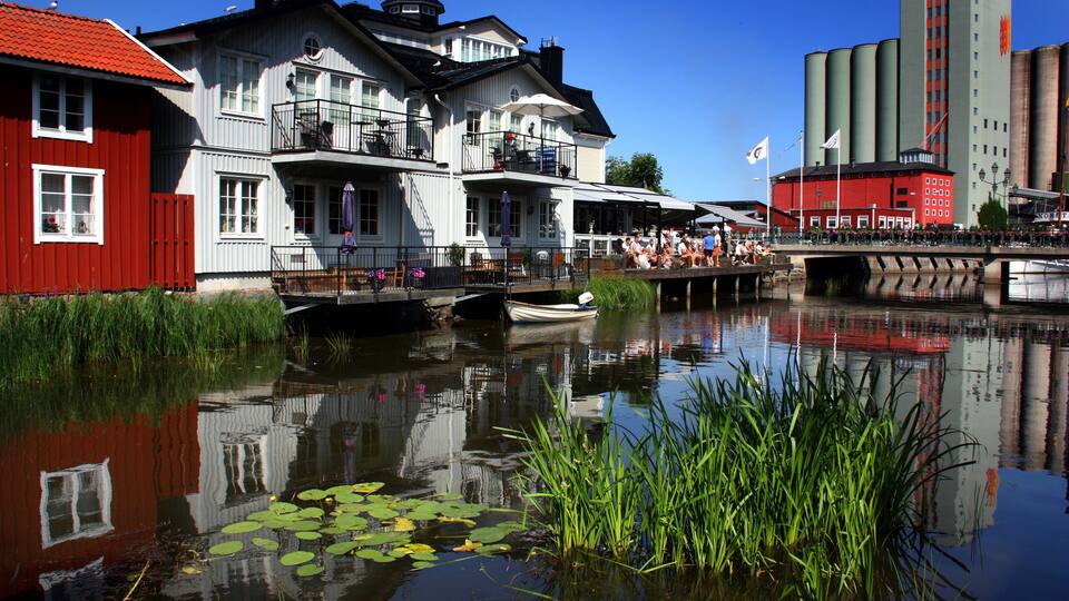 A canal with a red building, a white building with a balcony, and a large industrial structure.