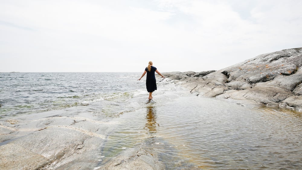 A person standing on rocky terrain by a body of water.