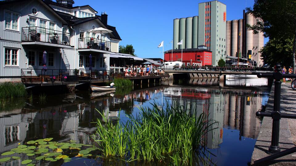 A canal with buildings, including a red industrial structure, and a bridge with people.