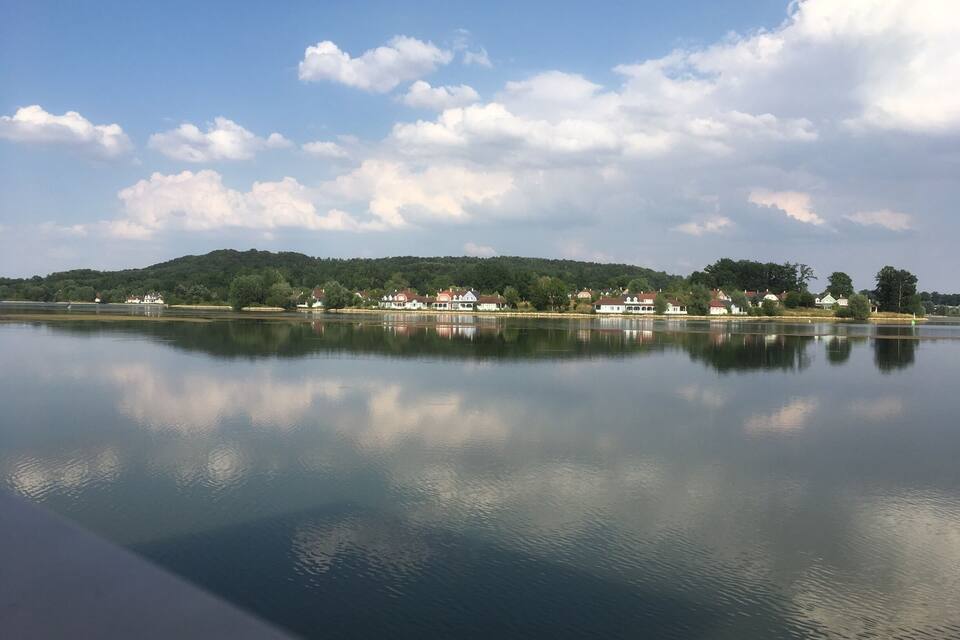A calm lake with a reflection of houses and trees on the opposite shore.