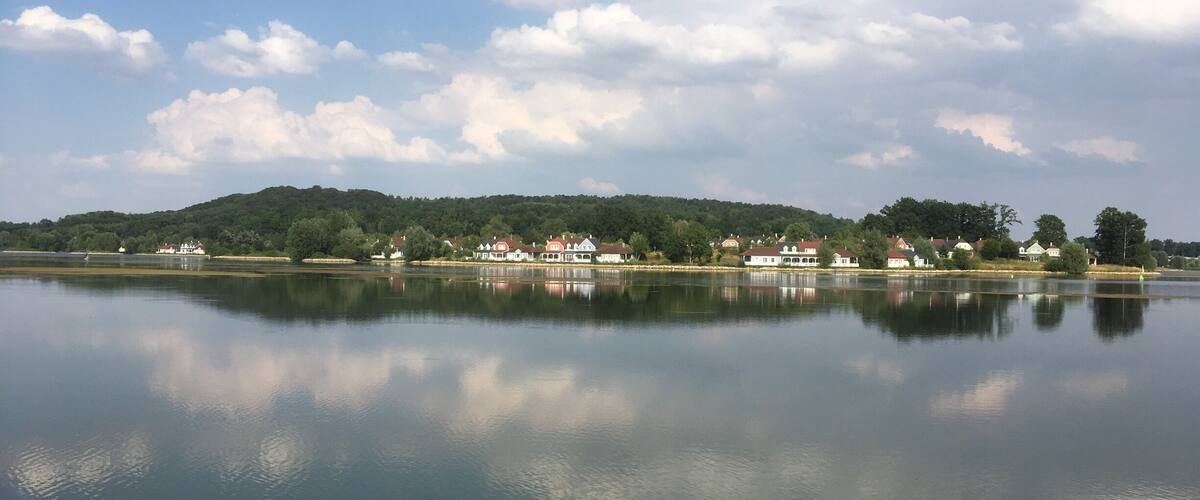 A calm lake with a reflection of houses and trees on the opposite shore.