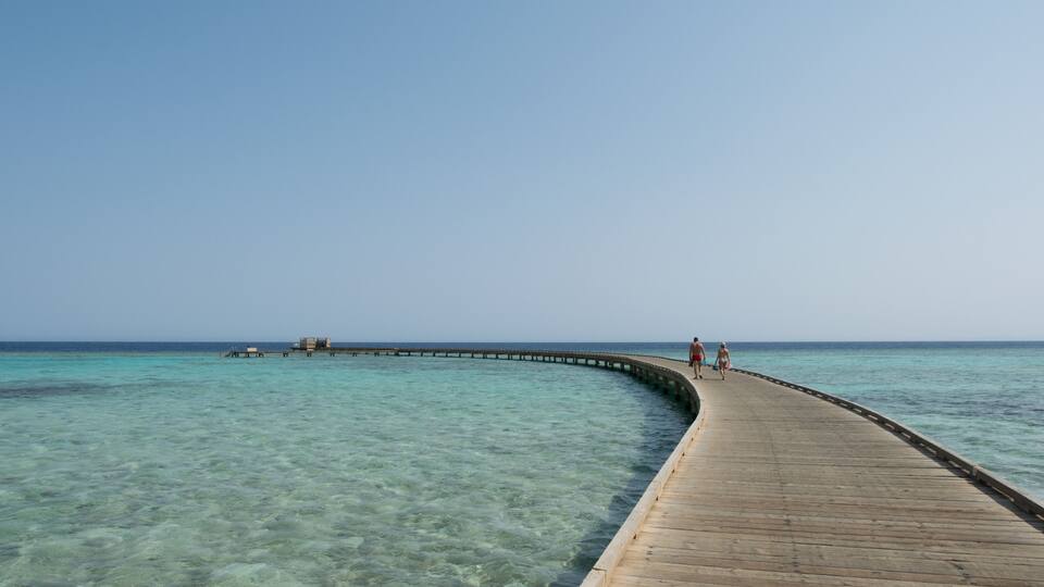 A wooden pier extending into clear turquoise water, with a few people walking along it.