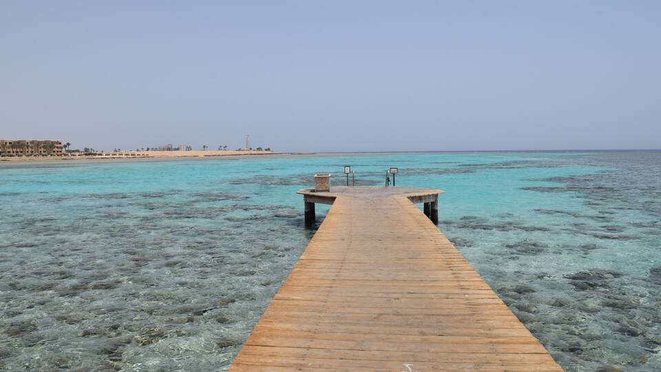 A wooden pier extending into a clear turquoise sea with rocky underwater terrain.