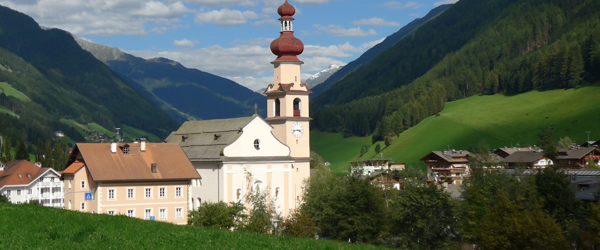 A church with a red onion dome, surrounded by green hills and mountains.