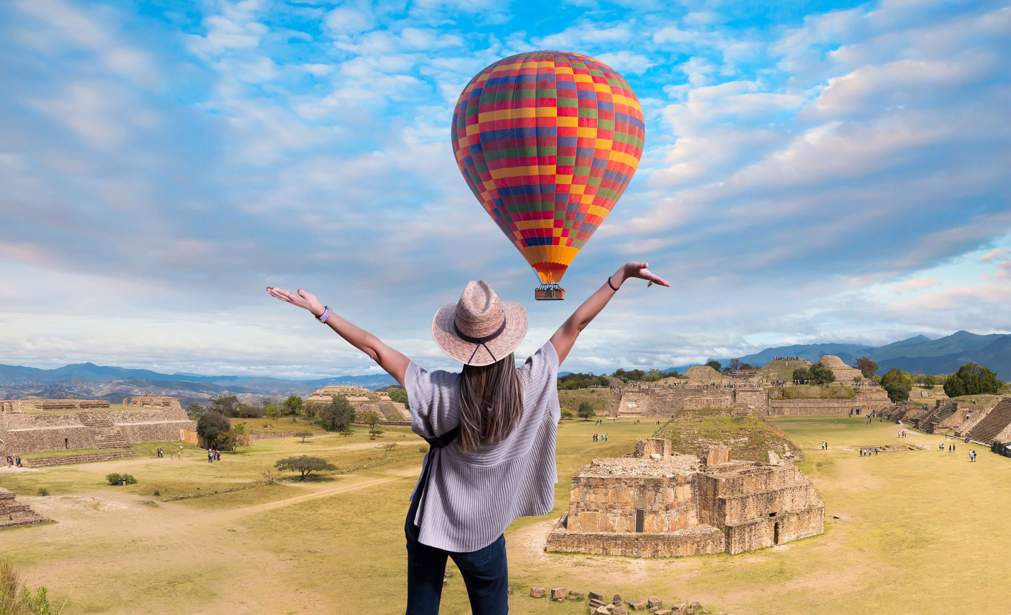 A person with arms raised, a colorful hot air balloon, and ancient ruins in the background.