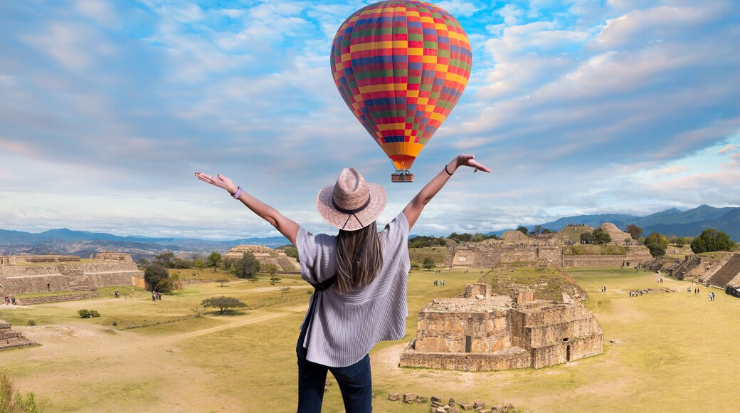 En person med armene i vejret, en farverig luftballon og gamle ruiner i baggrunden.