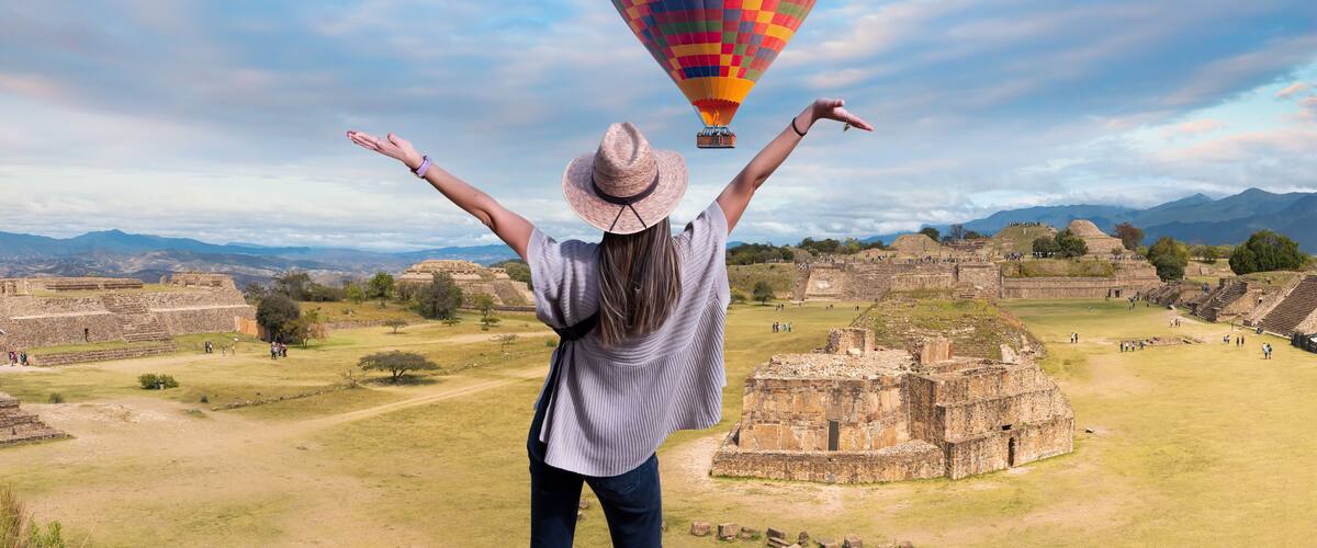 En person med armene i vejret, en farverig luftballon og gamle ruiner i baggrunden.
