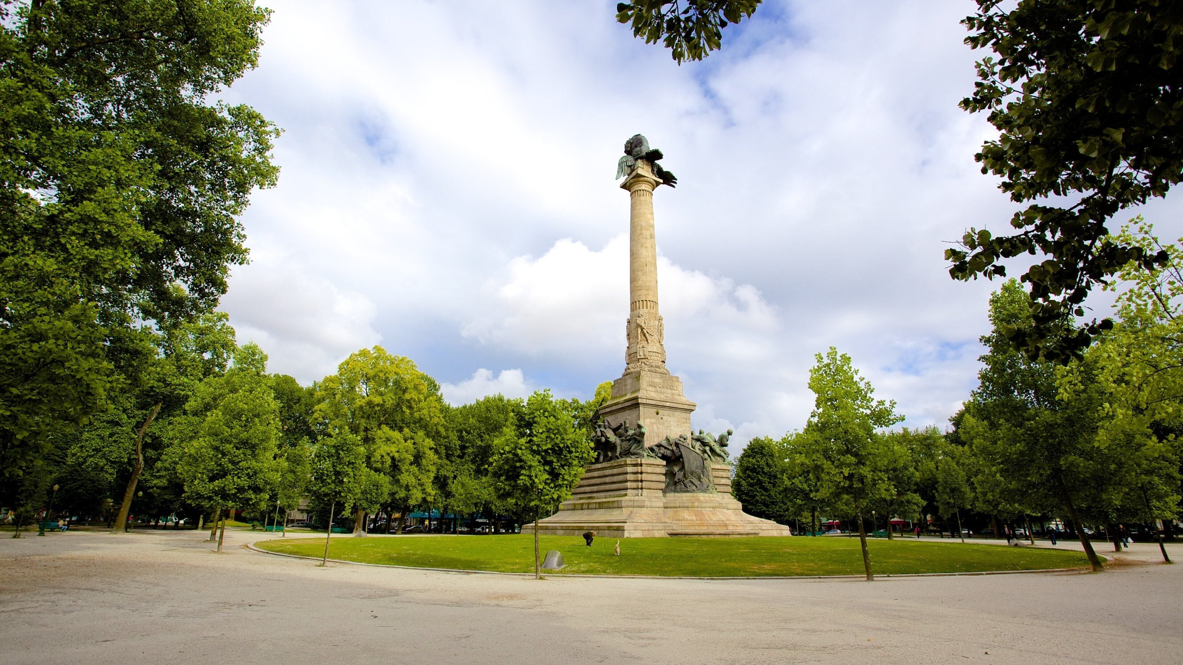 Un monument alt amb una estàtua a la part superior, envoltat d'arbres i una zona verda.