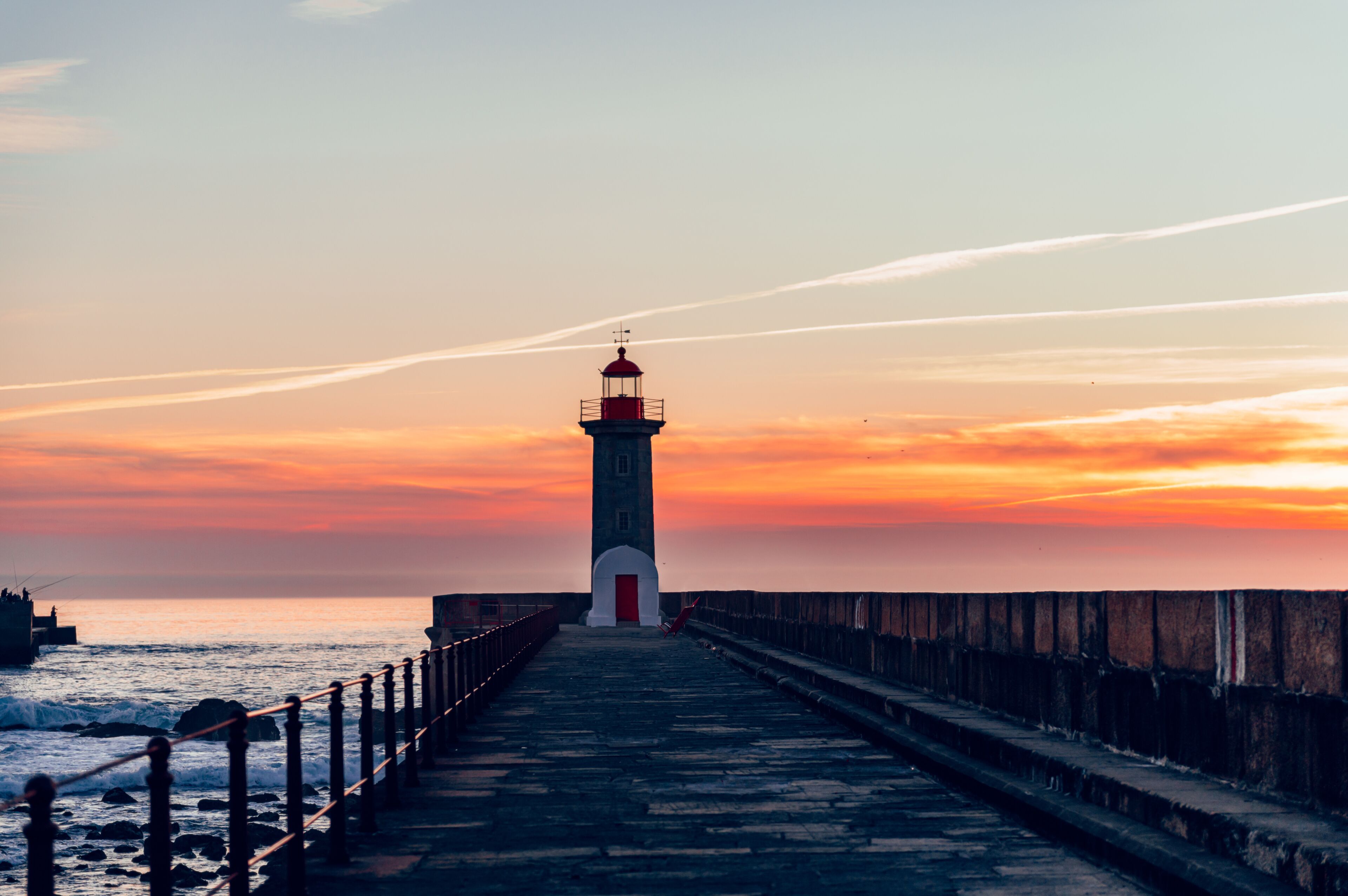 Un phare au coucher du soleil, avec une passerelle en bois menant à sa base.