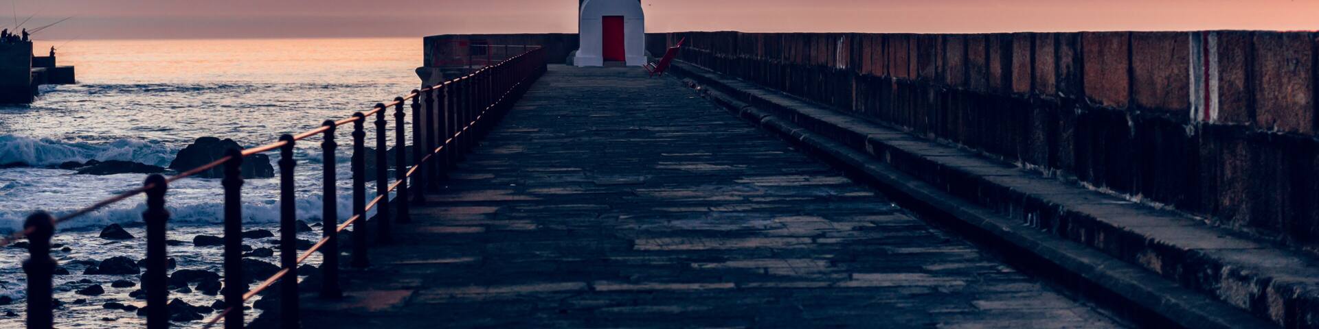 A lighthouse at sunset with a wooden walkway leading to it.