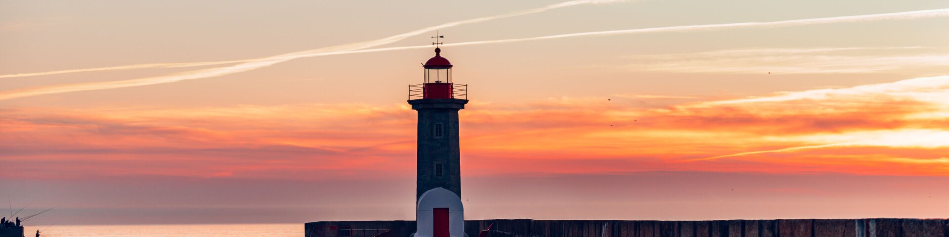Un phare au coucher du soleil, avec une passerelle en bois menant à sa base.