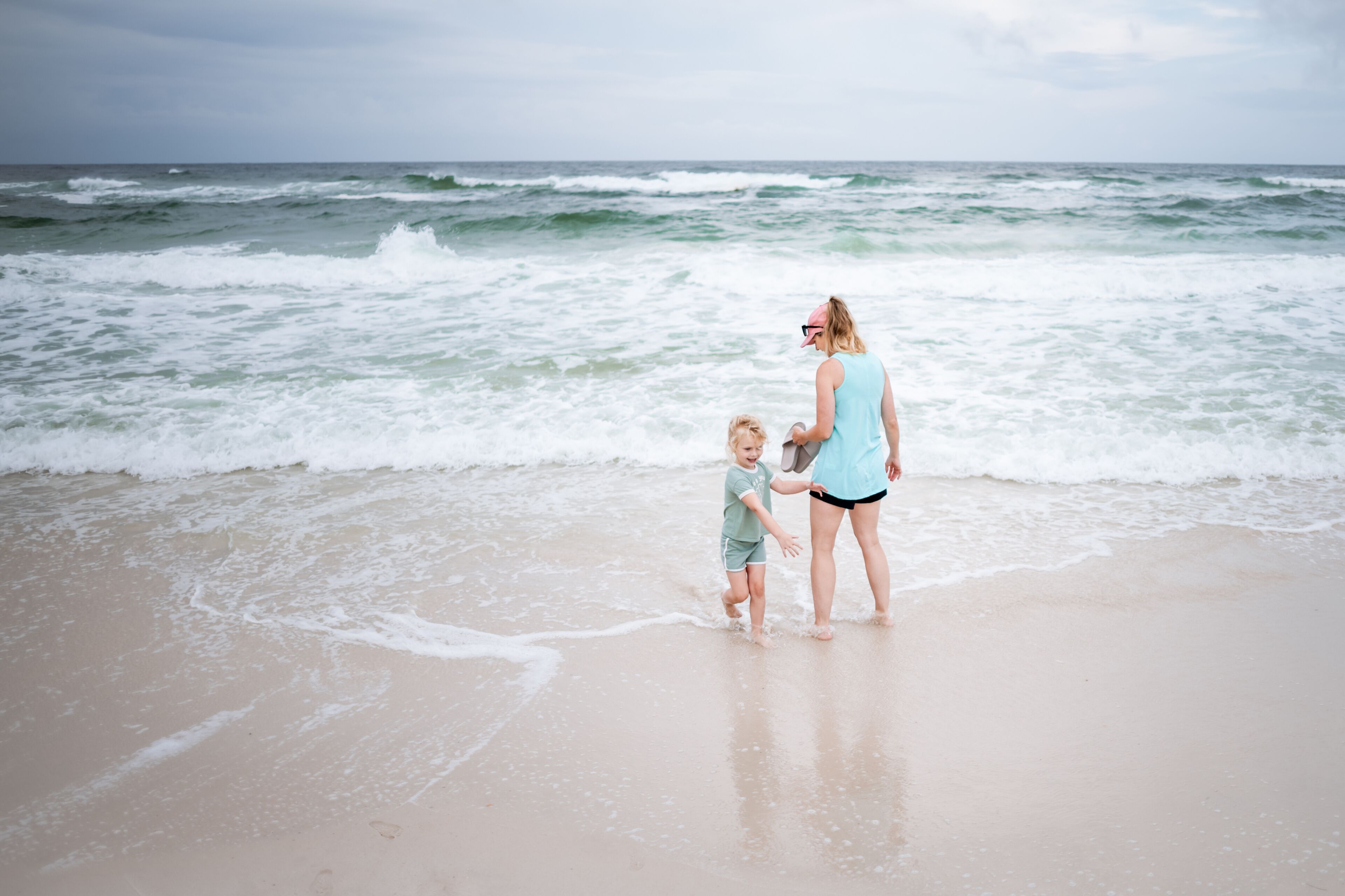 A beach with waves and a person and child near the water.
