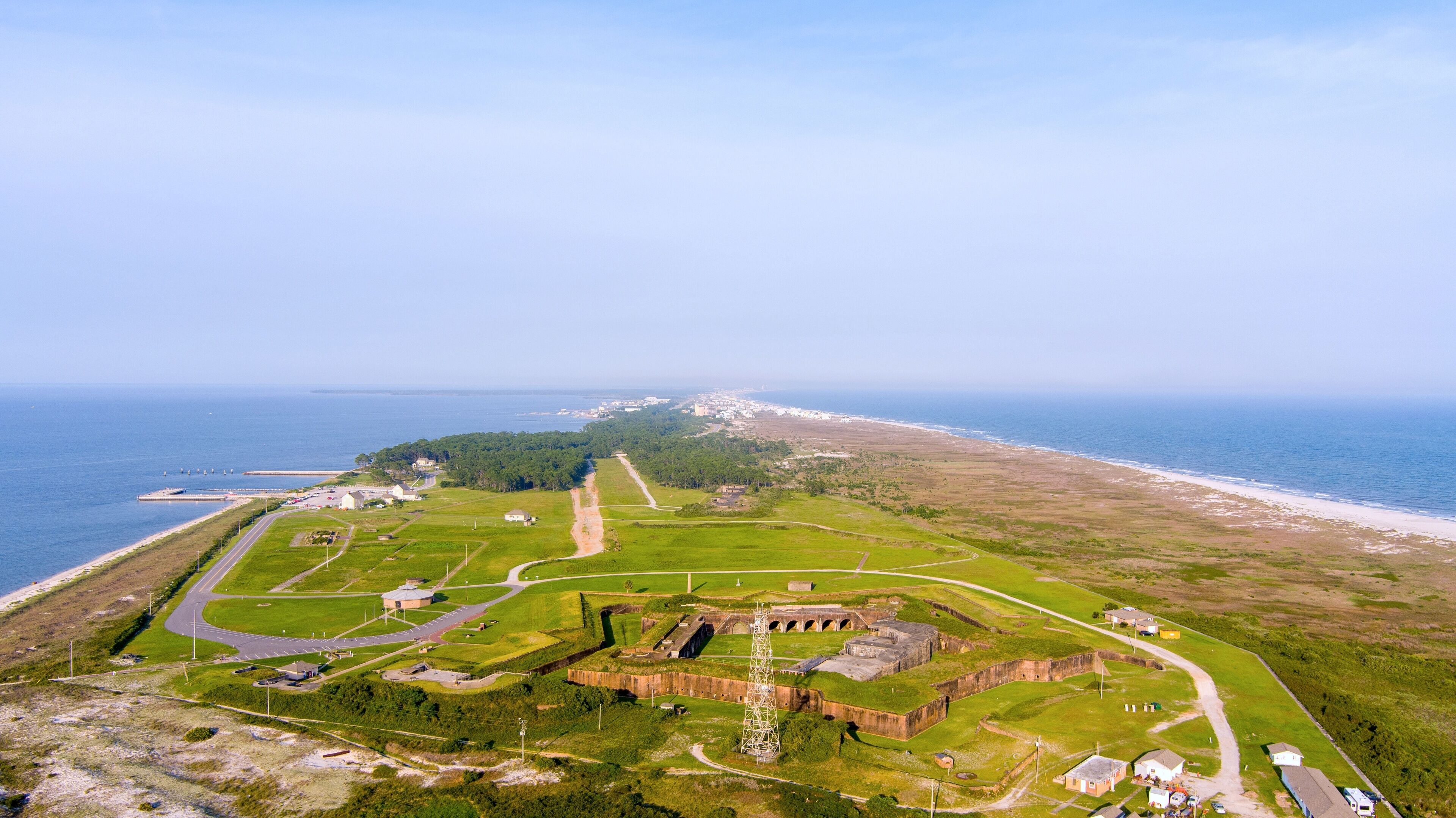 An aerial view of a coastal fort with surrounding green fields and a beach.