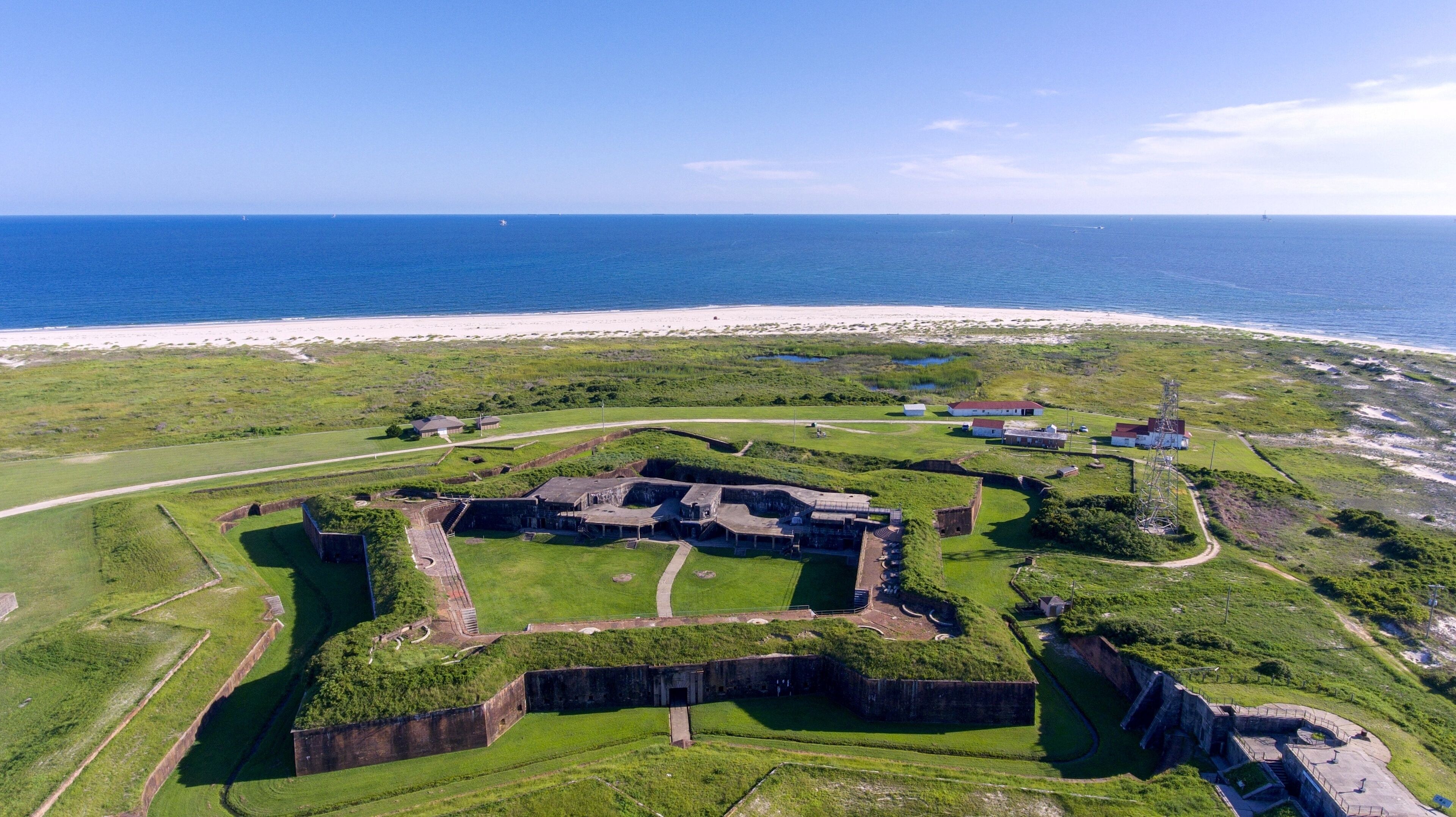 An aerial view of a coastal fort with surrounding grassy fields and a beach in the background.