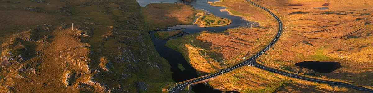 A winding road through a mountainous landscape with multiple lakes and a distant mountain range.