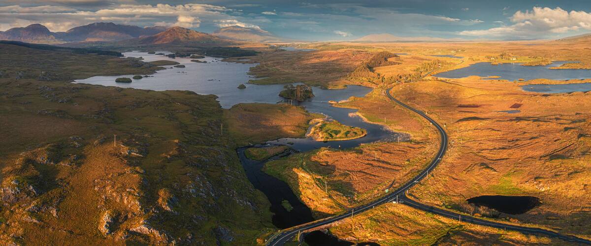 A winding road through a mountainous landscape with multiple lakes and a distant mountain range.