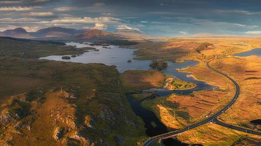 A winding road through a mountainous landscape with multiple lakes and a distant mountain range.