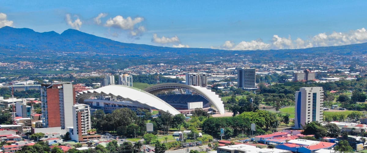 A cityscape with a stadium, buildings, and mountains in the background.