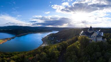 A panoramic view of a lake surrounded by hills, a castle, and a clear sky.