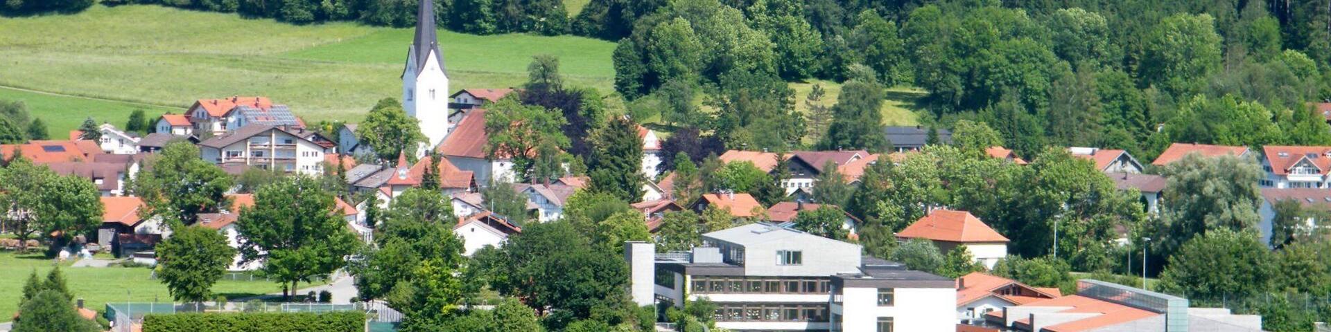 A rural landscape with rolling hills, a church with a tall steeple, and residential buildings with red roofs.