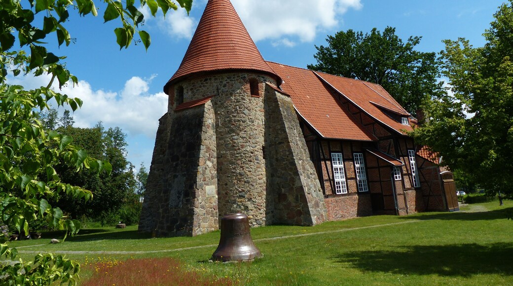 A church with a conical roof and stone walls, surrounded by greenery and a clear sky.