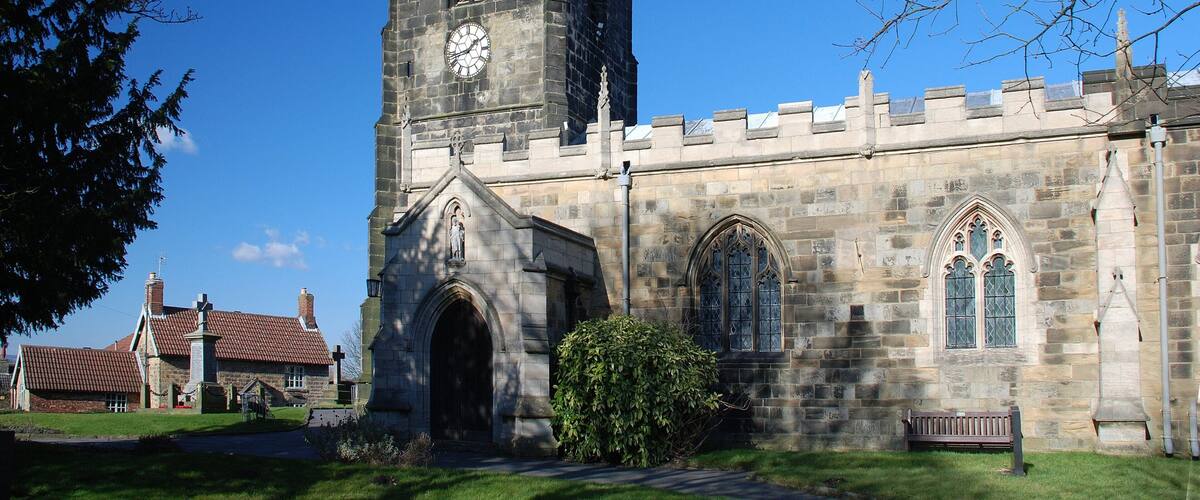 A historic church with a tall clock tower, arched windows, and a statue at the entrance.