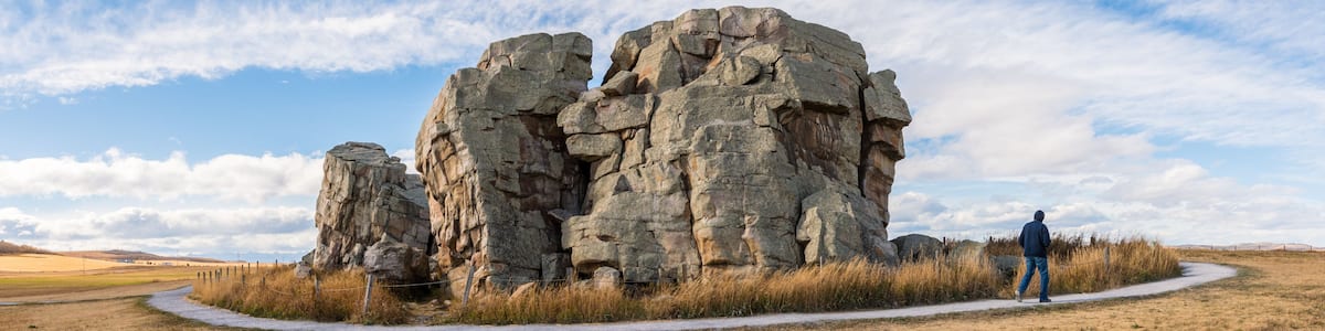 Big Rock Erratic Okotoks tourist destination giant boulder in the prairies landscape at sunset golden hour. Person walking on pathway at point of interest panorama