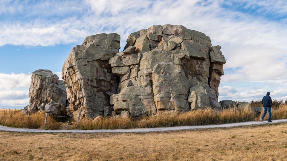 A large rock formation with a person walking nearby.
