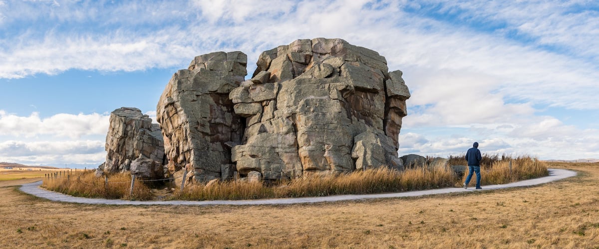 A large rock formation with a person walking nearby.