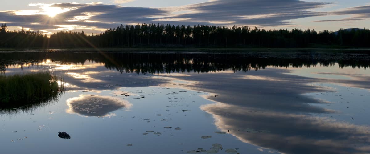 A sunset over a calm lake with reflections of the sky and trees.