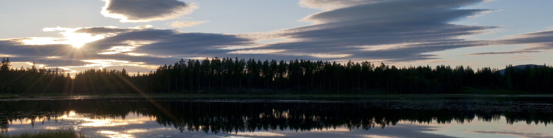 A sunset over a calm lake with reflections of the sky and trees.