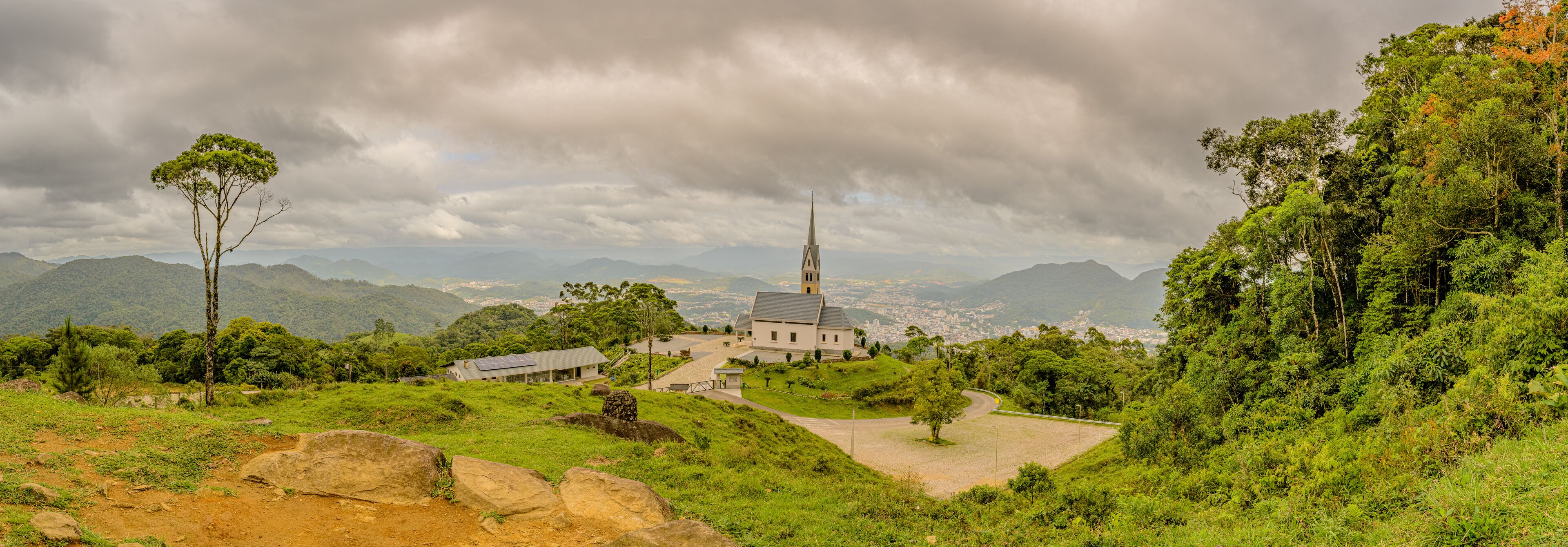 A church surrounded by lush greenery and mountains under a cloudy sky.