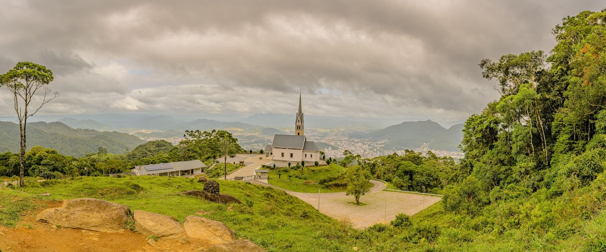 A church surrounded by lush greenery and mountains under a cloudy sky.