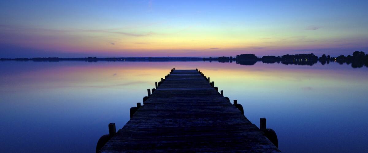 A wooden pier extending into calm waters at dusk with a clear sky above.