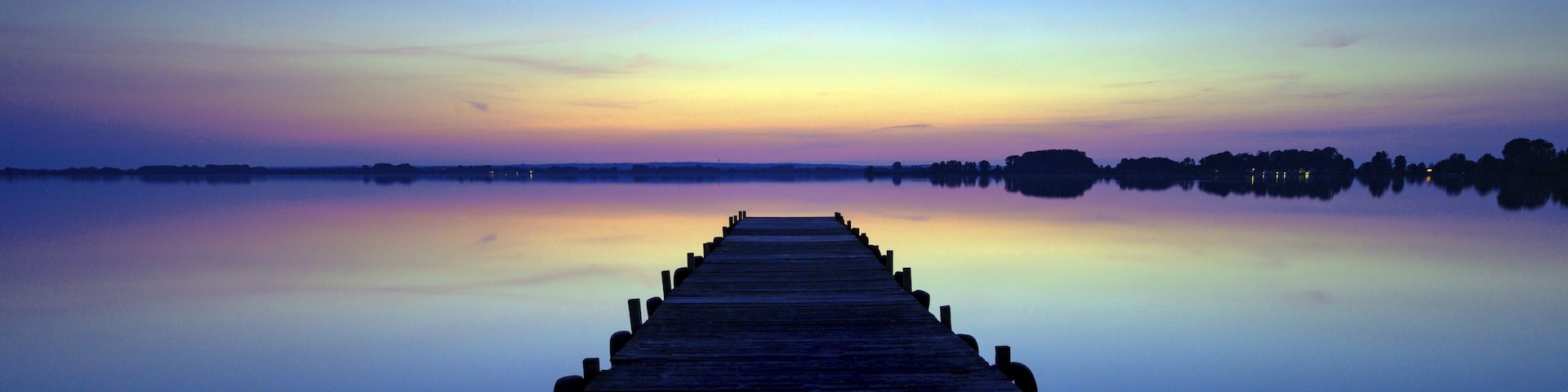 A wooden pier extending into calm waters at dusk with a clear sky above.