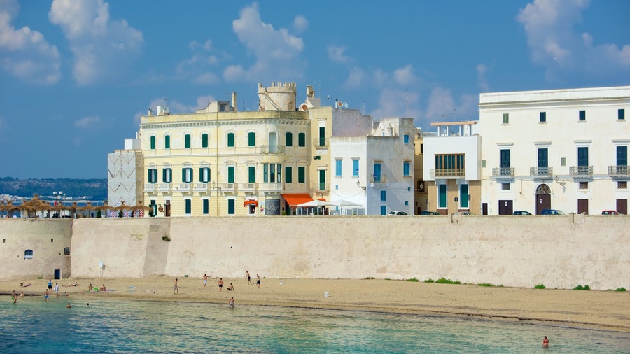 Un pueblo costero con edificios históricos, una playa de arena y aguas azul turquesa.