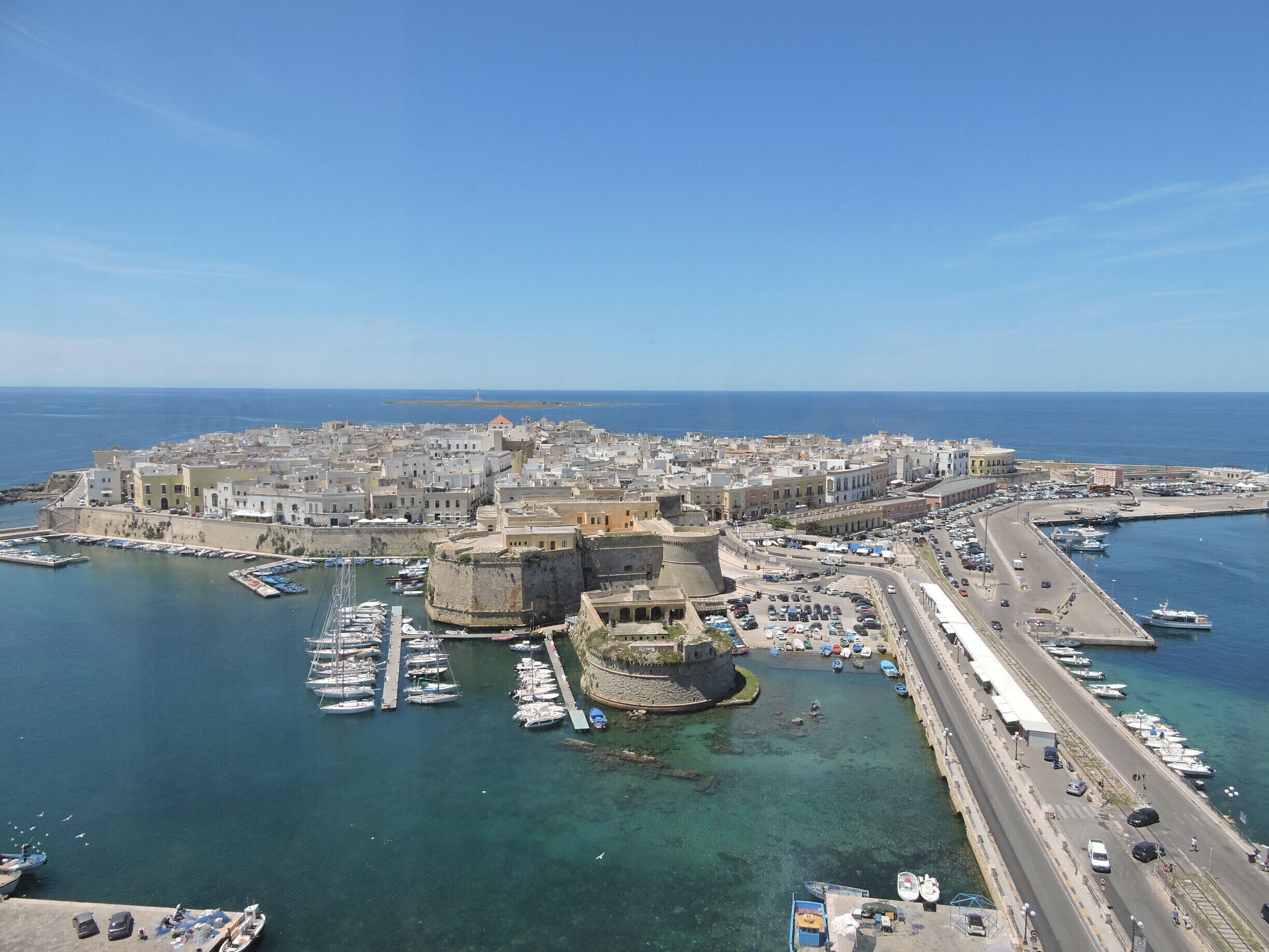 A coastal town with a fortified castle, marina, and a road leading to the sea.