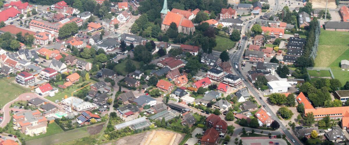 An aerial view of a town with red-roofed houses, a church with a green steeple, and a mix of residential and commercial buildings.