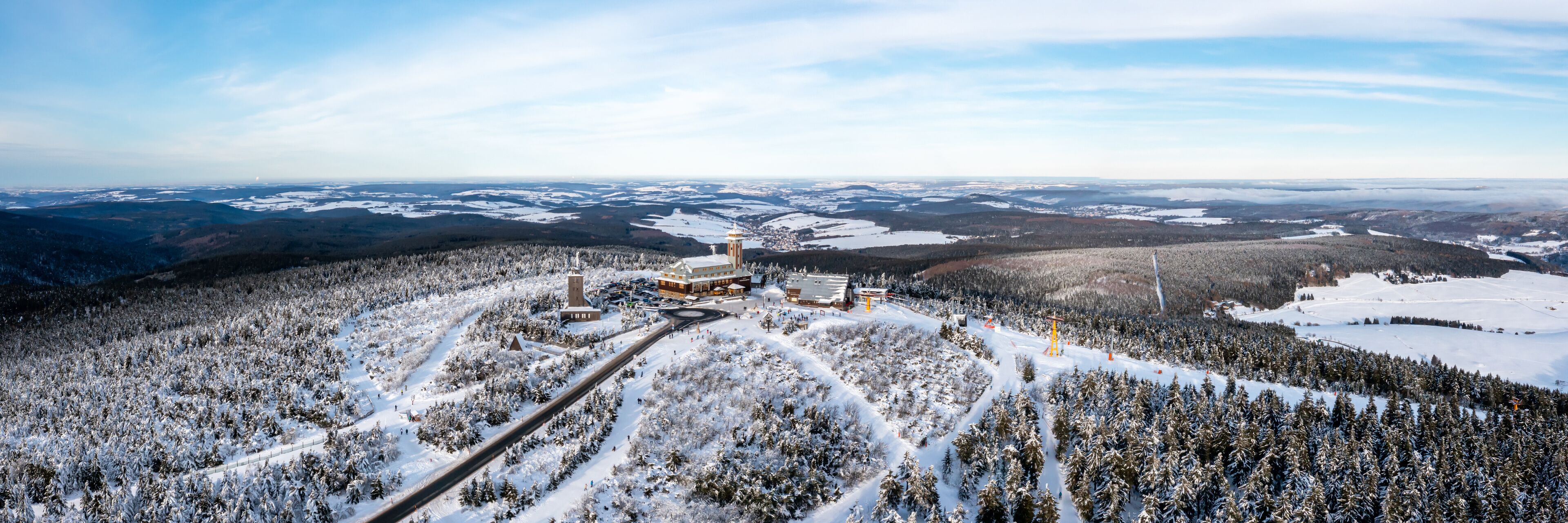 A snow-covered landscape with a large building complex, a ski slope, and a forested area.