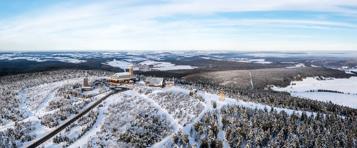 A snow-covered landscape with a large building complex, a ski slope, and a forested area.