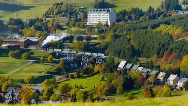 A scenic railway bridge, lush greenery, and residential buildings in a hilly landscape.