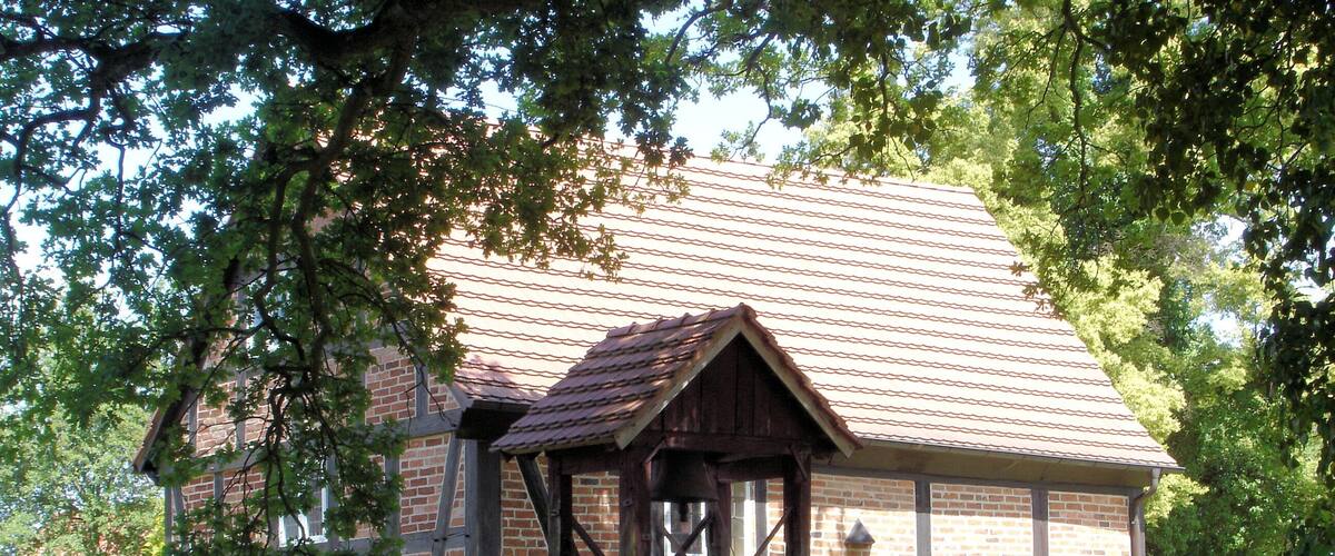A traditional wooden building with a tiled roof, surrounded by well-maintained hedges and a grassy lawn.