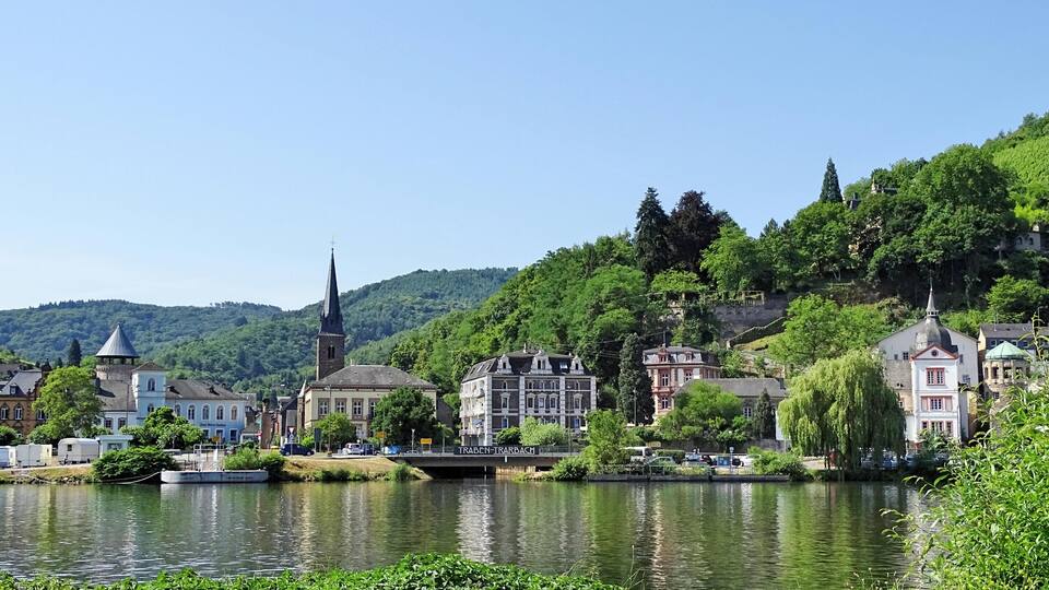 A riverside town with historic buildings, a church, and lush greenery.