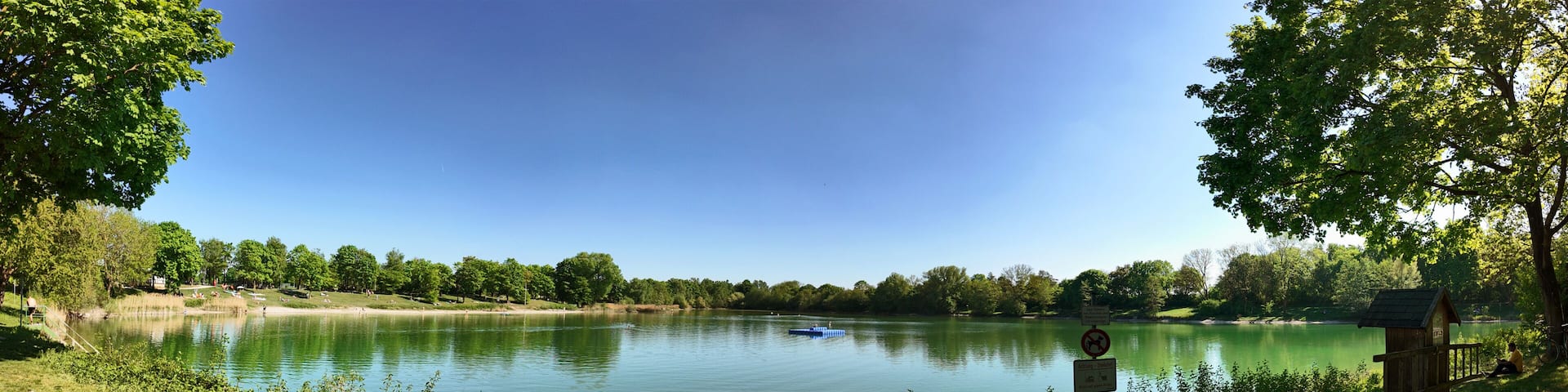 A calm lake surrounded by trees and a wooden structure on the right.