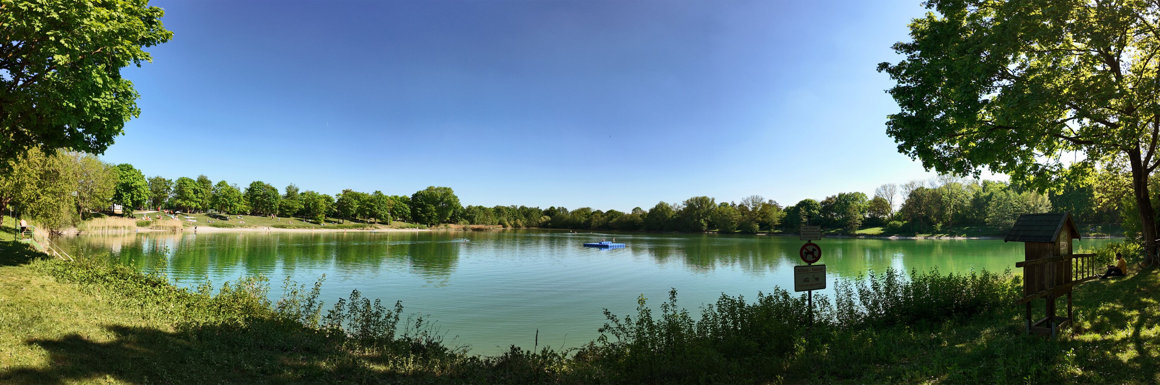 A calm lake surrounded by trees and a wooden structure on the right.