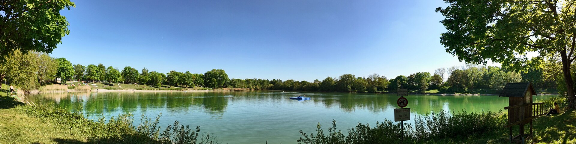 A calm lake surrounded by trees and a wooden structure on the right.