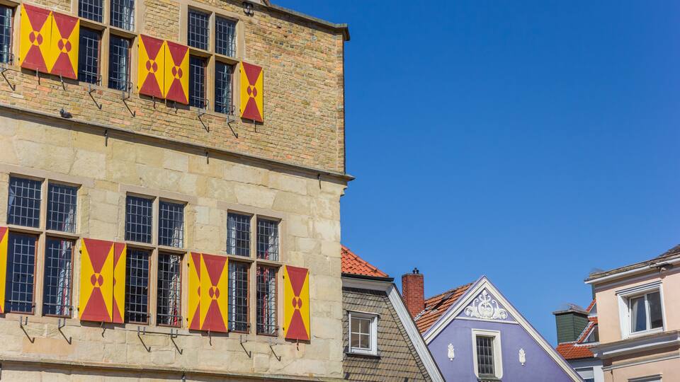 A historic building with red and yellow window shutters and a tiled roof.