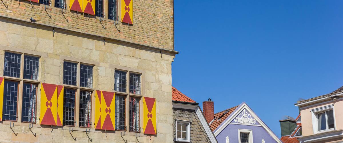 A historic building with red and yellow window shutters and a tiled roof.
