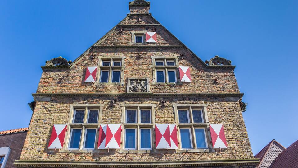A historic building with a steeply pitched roof, multiple windows, and decorative red and white patterns on the facade.